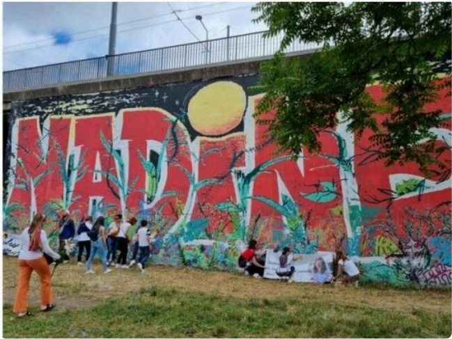Mural en hommage à Nadine — lettres rouges devant lesquelles des proches sont rassemblés